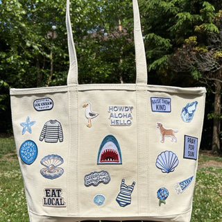 Beige tote bag with various appliqués on a wooden stool outdoors.