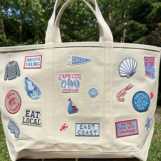 Beige tote bag with various embroidered patches on a wooden table outdoors.