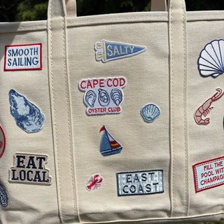 Beige tote bag with various embroidered patches on a natural background