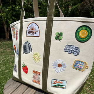 Beige tote bag with various patches on a wooden stool outdoors