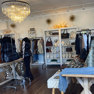 Interior of a clothing store with racks, tables, and a chandelier.