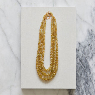 Gold beaded necklace on a white card with a marble background