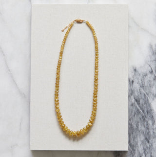 Yellow beaded necklace on a white card with a marble background