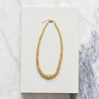 Yellow beaded necklace on a white card with a marble background