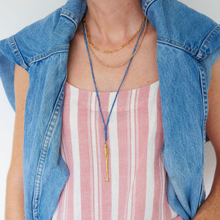 Person wearing a striped tank top, denim jacket, and layered necklaces.