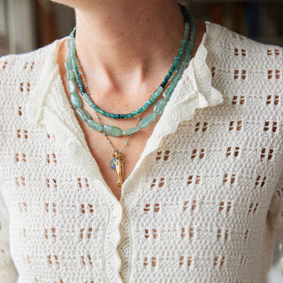 A close-up of a person wearing a cream open-knit button-up cardigan and layered turquoise and gold necklaces.