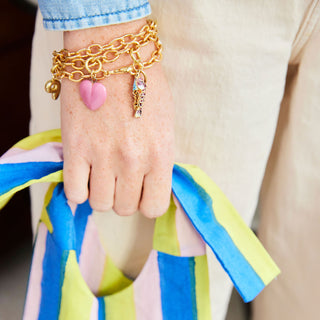 Gold bracelet with heart and key charm on a hand wearing a colorful striped garment.