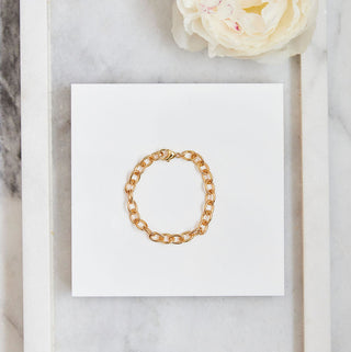 Gold bracelet on a white card inside a framed picture with a white flower on a marble background