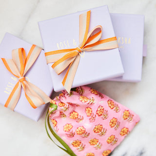 Gift boxes with orange ribbons and a pink floral pouch on a marble surface