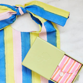 Colorful striped fabric with a bow and two small bags on a marble surface