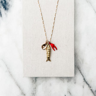 A gold chain necklace with a lobster and fish pendant, displayed on a textured white card over a white marble background.